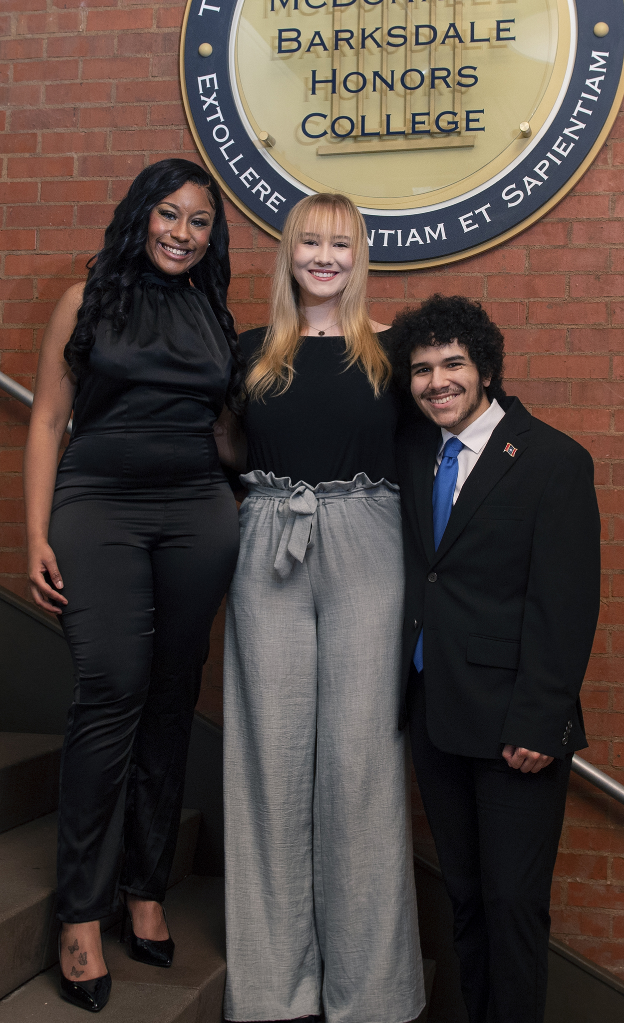 Jilkiah Bryant, Alex Bush, and Andy Flores pose smiling in front of the Sally Barksdale Honors College
